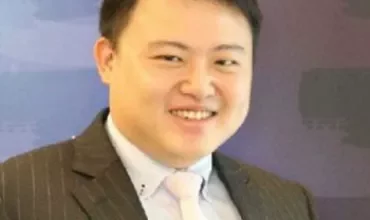 Portrait of a person smiling in a suit with a purple background.