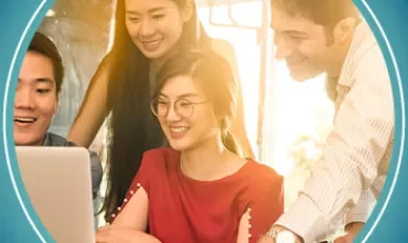 Group of four people smiling and collaborating around a laptop in an office setting.