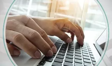 Hands typing on a laptop keyboard by a sunny window.