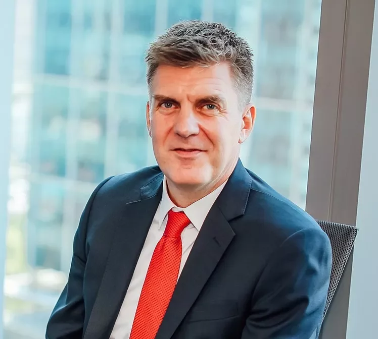 Man in a suit with a red tie sitting by a window.