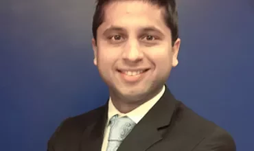 Man in a suit smiling against a blue background.