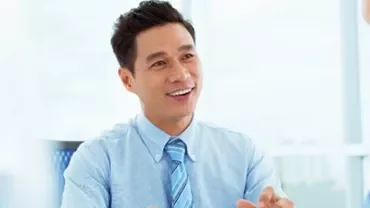 Man in blue shirt smiling during a meeting in a bright office.
