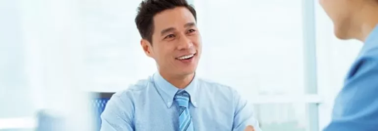 Man in blue shirt smiling during a meeting in a bright office.