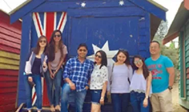 Group of people posing in front of a colorful beach hut with Australian flag decoration.