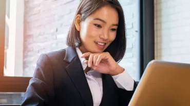Person in a suit working on a laptop near a sunlit window.