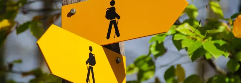 Two yellow hiking trail signs with black hiker icons on a wooden post