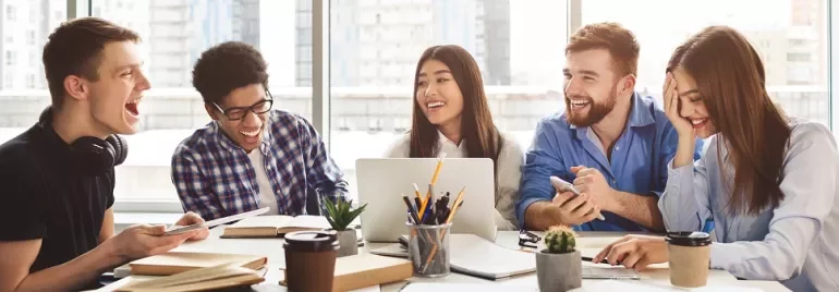 Group of diverse students laughing and studying together in a bright room.