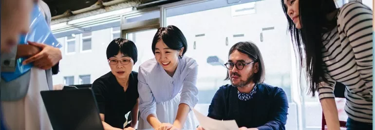 A diverse team collaborating around a laptop in a bright office setting.