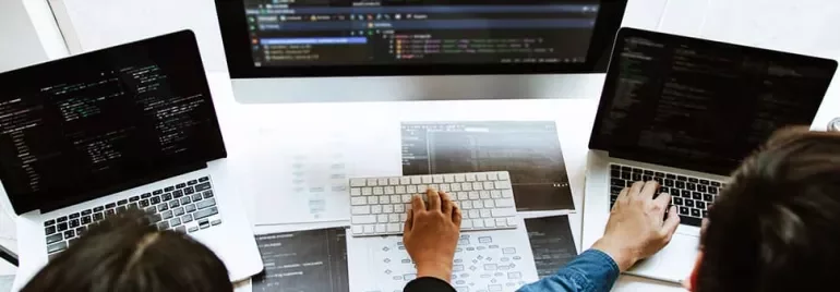 Three people working on laptops with code on the screens.