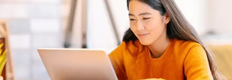 Woman in orange sweater using a laptop at a desk.