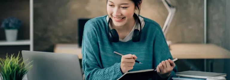Woman smiling while studying with a laptop at a desk.