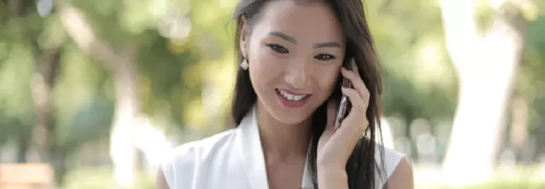 Woman smiling while talking on a phone outdoors.