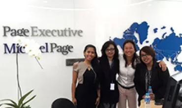 Group of four people smiling in an office with a world map on the wall.