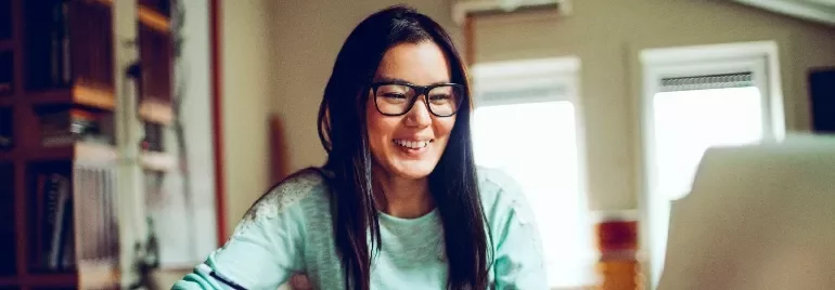 Smiling woman with glasses working on a laptop at home.