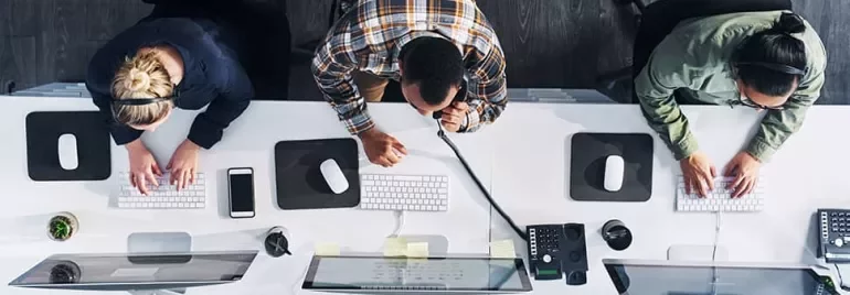 Overhead view of three people working at computers in an office.