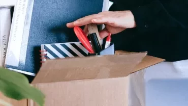 Person packing stationery and books into a cardboard box.