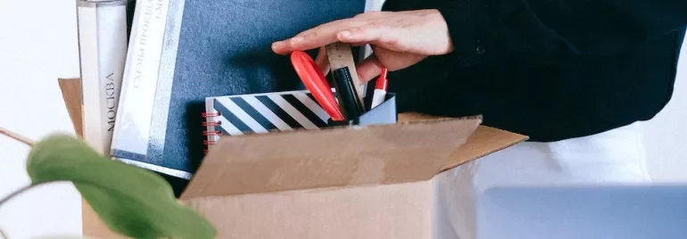 Person packing stationery and books into a cardboard box.