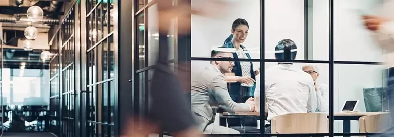 Business meeting in a modern glass-walled office with people discussing.