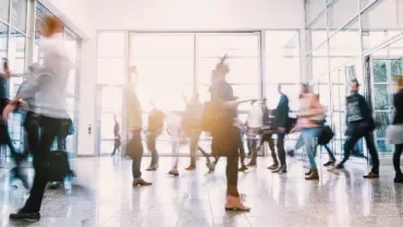 Blurred motion of people walking through a modern glass entrance.