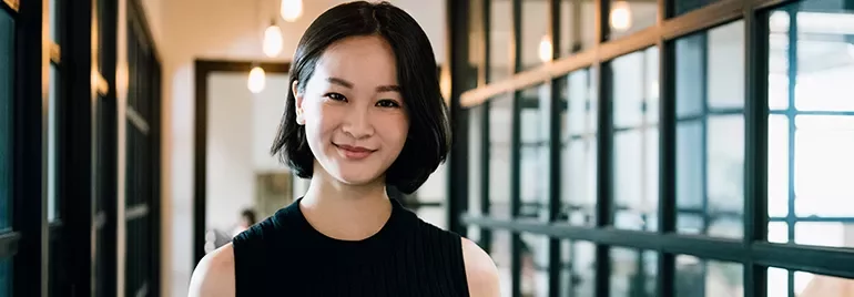 Person smiling in a modern office hallway with glass walls.