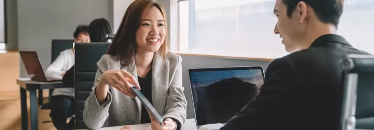 Two professionals having a conversation in an office setting with laptops.