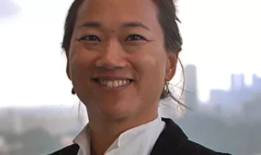Portrait of a smiling person in a suit with a city skyline background.