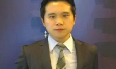 Man in a suit with a patterned tie standing against a blue background.