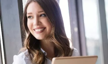 Woman smiling by a window with a tablet